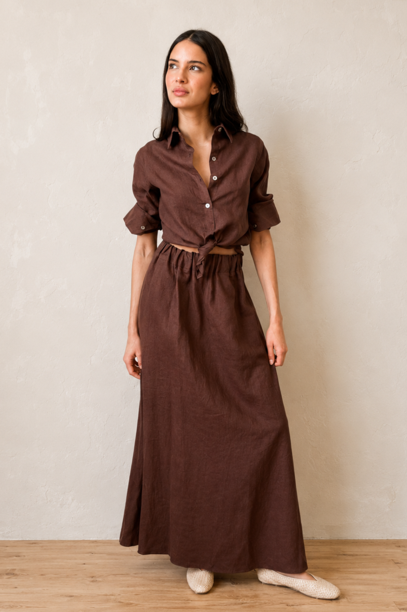 Woman wearing a brown linen shirt and brown linen maxi skirt against a plain background